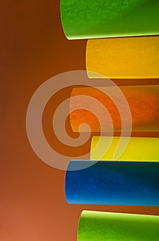 Vertical image of rolled coloured paper against orange background.Empty space