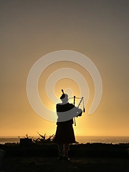 Vertical image of the silhouette of a bagpiper at sunset in Carmel, California in front of the Pacific Ocean
