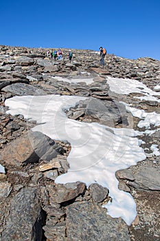 Vertical image of the slope that goes to Mulhacen with hikers going up and a bit of snow in the foreground photo