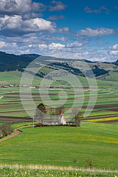 Vertical image, small catholic church on hilltop surrounded by green agricultural field