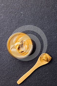 Vertical image of spoon and bowl with peanut butter on dark grey surface