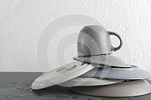 Closeup of stack clean and wet plates, cup on the grey table against white wall.Empty space