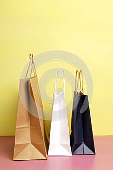 Vertical image.Three shoppin bags on the pink desk against bright yellow wall