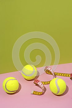 Vertical image of three tennis balls,measuring tape on the pink surface against green background.Empty space