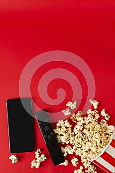 Vertical image.Top view of smartphone, clicker and popcorn on the red background.Empty space