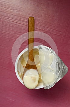 Vertical image.Top view of wooden spoon full of tasty fresh yogurt on the opened cup. pink background