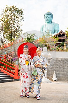 Vertical image of two Asian women wear japanese style dress with one hold red umbrella and stand in front of stair to green big