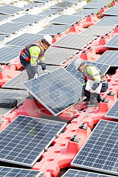 Vertical image of two technician workers help to installation or set up solar cell panels that base over area of water reservoir
