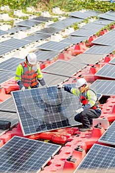 Vertical image of two technician workers help to set up or install solar cell panel into base over water reservoir