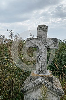 Vertical image. Unnamed gravestone on old abandoned city cemetery. Weathered stone cross on abandoned graveyard