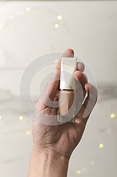 Vertical image.Woman holding bottle of beige colored nail polish against bokeh lights