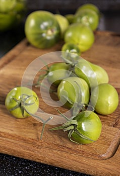 Vertical image.Wooden cutting board and fresh juicy unripe tomatoes on it