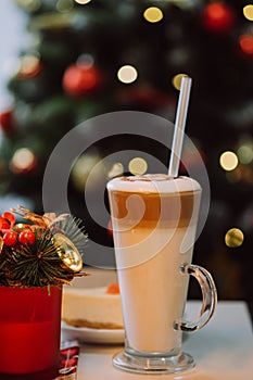 Vertical images of cup of milkshake with straw on white table against background decorated Christmas tree. Concept festive drinks