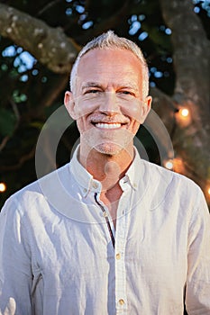 Vertical individual portrait of handsome mature man with gray hair looking and smiling at camera. Happy middle aged male