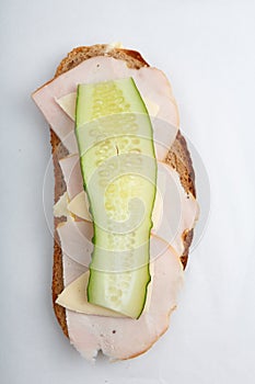 Vertical isolated close up top view shot of a single white bread turkey ham and cheese sandwich with a slice of cucumber on top on