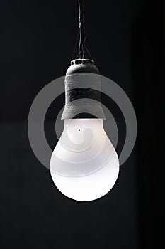 Vertical isolated shot of a hanging white lightbulb on a black background