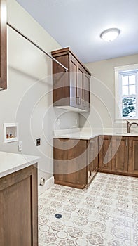Vertical Kitchen interior with brown wooen cabinets white countertops sink and window
