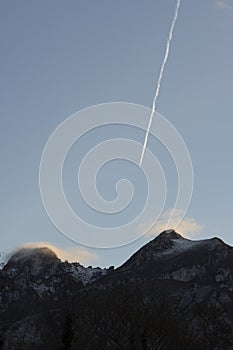 Vertical landscape of airplane flying above mountain peaks with fog at sunset