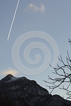 Vertical landscape of airplane flying above mountain peaks with fog at sunset