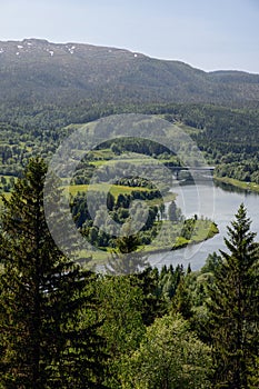 A vertical landscape photo of Elstad in Trondelag, Norway, capturing a river\'s bend surrounded by dense forests