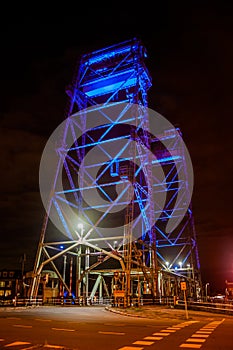 Vertical lift bridge in a town near Gouda, Holland, over the canal Gouwe is illuminated by blue light beams at night.