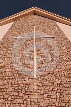 Vertical low-angle closeup of a stone wall of a church with a huge cross on it