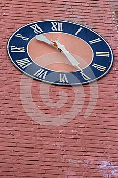 Vertical low angle of an old clock with roman numbers on a brick wall