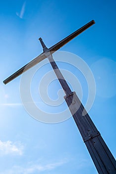 Vertical low angle shot of a big wooden cross against a blue sky.