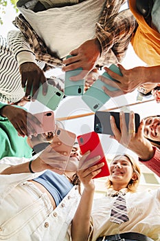 Vertical low angle view of a big group of smiling multiracial teenagers addicted to smart phones, watching funny videos