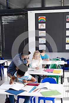 Vertical of male teacher and happy girl talking at her desk in diverse school class, copy space