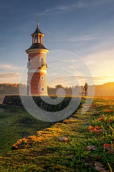 Vertical of a man walking his dog and sightseeing Leuchtturm in Moritzburg, Germany at sunset
