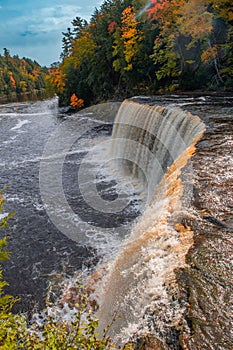 Vertical of the mesmerizing Tahquamenon Falls waterfall in Michigan surrounded by autumn foliage