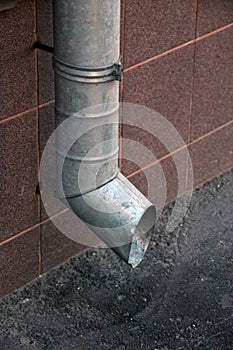 Vertical metal tinplate drain pipe with bell at wall on street closeup