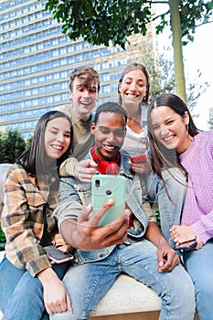 Vertical. Multiracial group of friends enjoying and smiling using a cellphone app. Diverse teenagers having fun watching