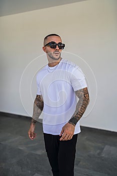 Vertical of a muscular tattooed young caucasian guy posing in simple urban clothes.