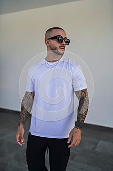 Vertical of a muscular tattooed young caucasian guy posing in simple urban clothes.