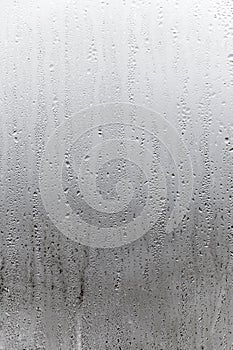 Vertical natural background, condensation on glass with drops flowing down, humidity and foggy blank. Outside , bad weather, rain