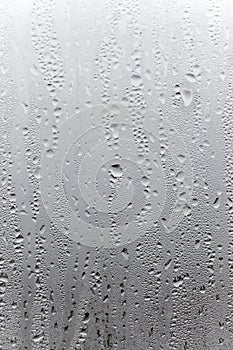 Vertical natural background, condensation on glass with drops flowing down, humidity and foggy blank. Outside , bad weather, rain