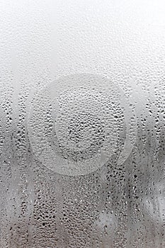 Vertical natural background, condensation on glass with drops flowing down, humidity and foggy blank. Outside , bad weather, rain