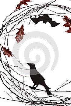 Vertical Ñomposition of branches, red leavese and carved raven on white background.