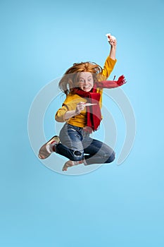 Vertical ortrait of young excited girl in a jump isolated over blue background. Recovering from a flue, cold