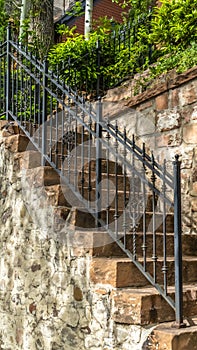 Vertical Outdoor staircase with stone steps and black metal railing against a fence