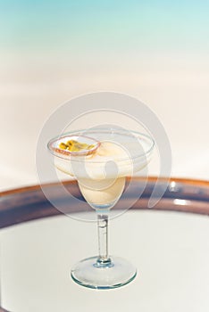 Vertical photo of Banana Daiquiri drink with passion fruit on the glass table ocean background at the beach