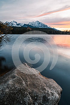 Vertical photo of beautiful lake in autumn scenery with amazing snowy mountains on background. Strbske pleso in High Tatras in