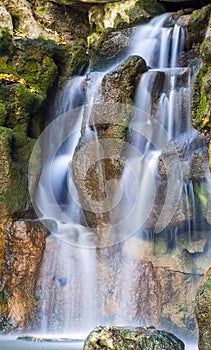 Vertical photo of beautiful waterfall in park with green moss on