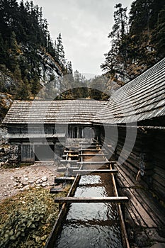 Vertikální fotografie krásné dřevěné chaty hluboko v lese - Mlyny Oblazy Slovensko. Starý dřevěný mlýn s kameny na pozadí