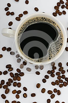 Vertical photo of black aromatic coffee with froth in a white mug among coffee beans in defocus on a white background