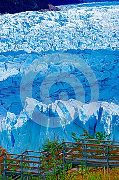 Vertical photo of the blue ice wall of a glacier with a stairs in front of it