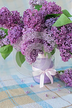 Vertical photo of a bouquet of flowers with lilac petals in a vase with a bow on a table with a checkered tablecloth