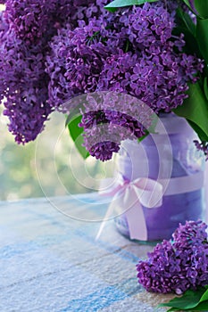 Vertical photo of a bouquet of flowers with lilac petals in a vase with a bow on a table with a checkered tablecloth